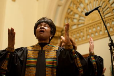 A black woman singing with hands raised at the front of a church