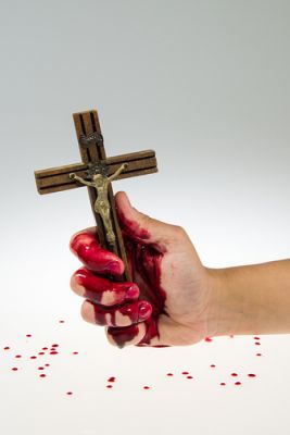 A bloody hand holding a religious figure of a wooden cross