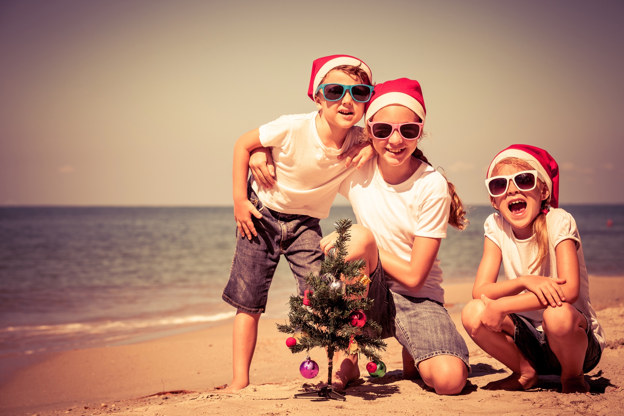 Children wearing Christmas hats on the beach.