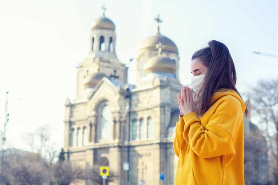 Woman praying with facemask in front of church