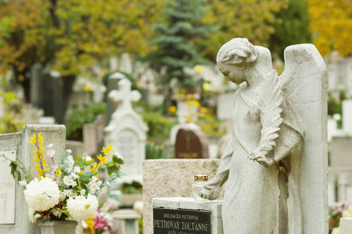 Angel statue beside graves and flowers in a cemetery on All Saints' Day
