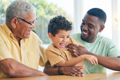 Grandfather, father, and son laughing together during a family moment at home.