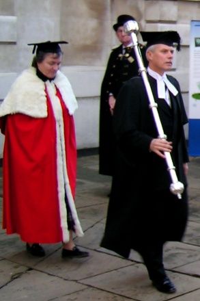 Graduate and university official in traditional academic dress during a Cambridge degree ceremony.
