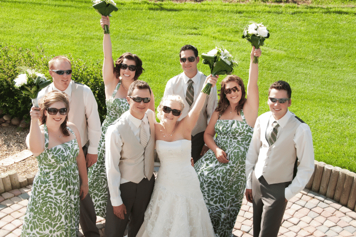 Couple celebrating with their wedding party outdoors as friends and family raise bouquets in the air.
