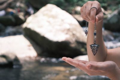 A divination pendulum being held over a hand in front of a stream.