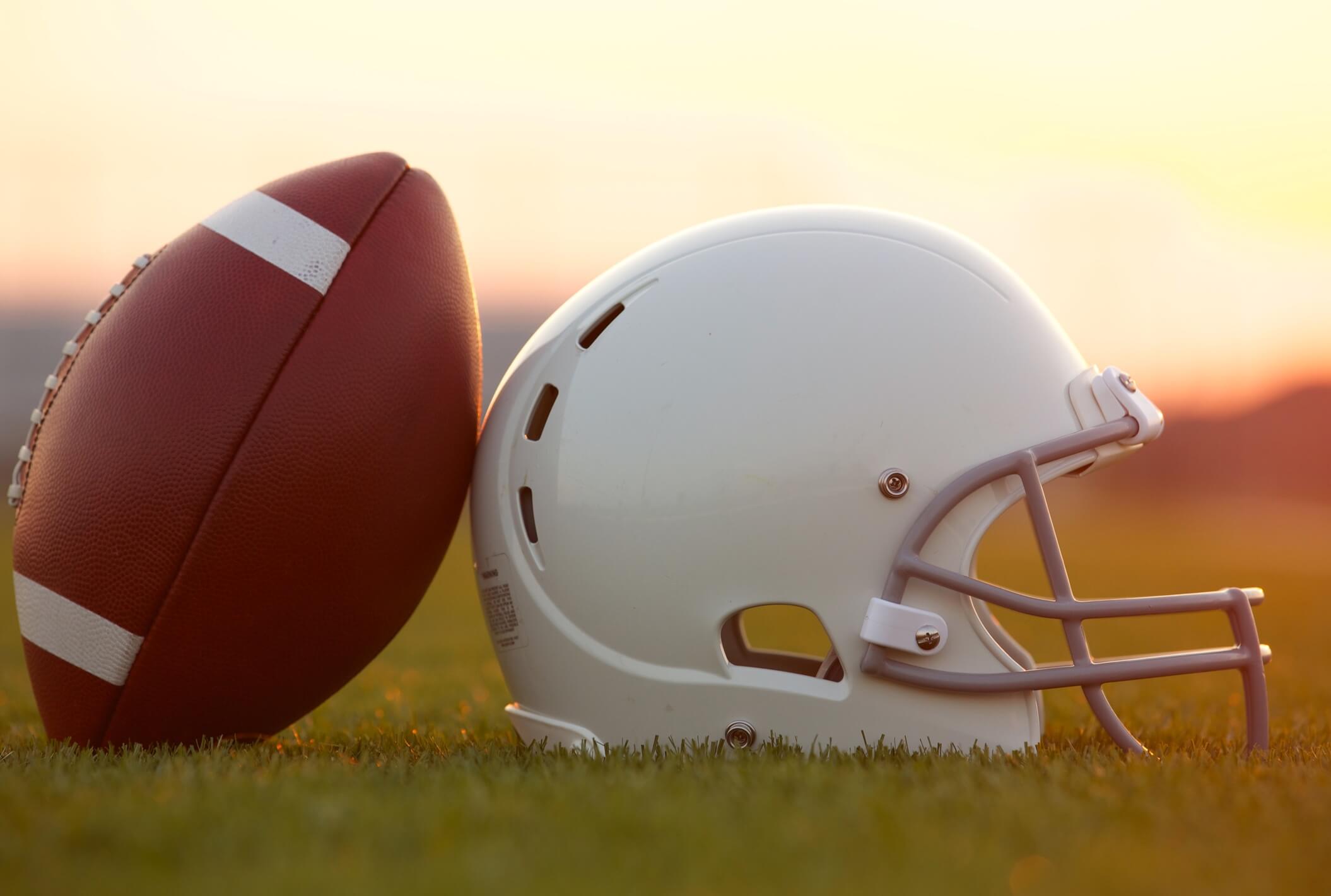 Football and Helmet on the Field at Sunset