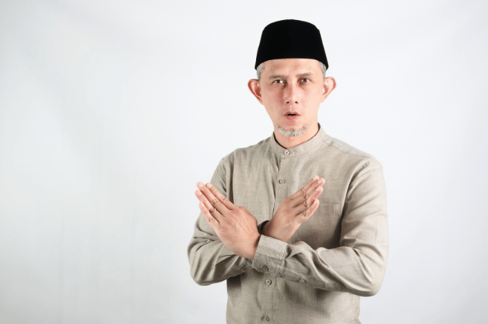 Man wearing traditional Muslim attire crossing his arms in a gesture of refusal.