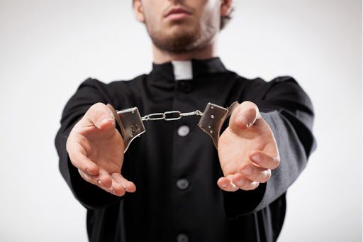 Handcuffed minister wearing black cassock