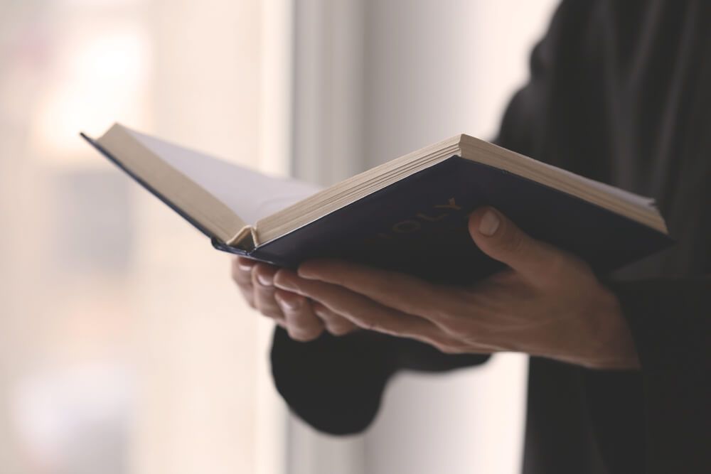 Hands holding the Bible as someone reads from it.