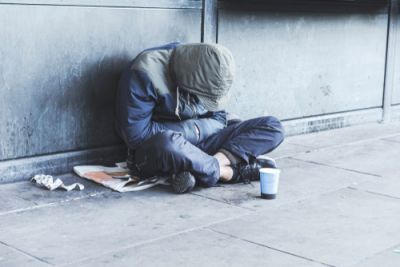A homeless man sitting on the sidewalk by himself