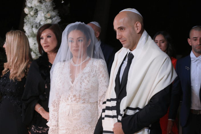 Bride and groom standing together during a Jewish wedding ceremony, with the groom wearing a tallit