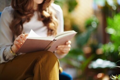 A red-haired woman reading a library book in a garden.