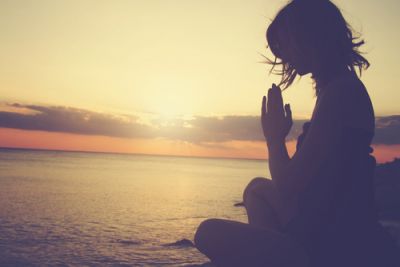 Meditation with hands closed together on a beach at sunset