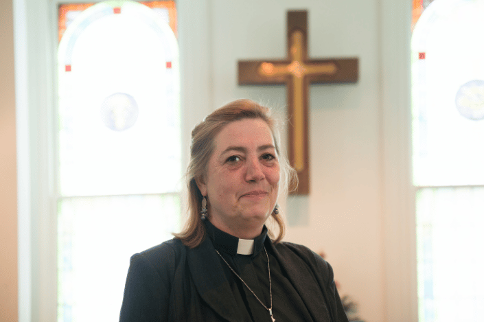 Minister wearing a clergy collar inside a church with a cross in the background