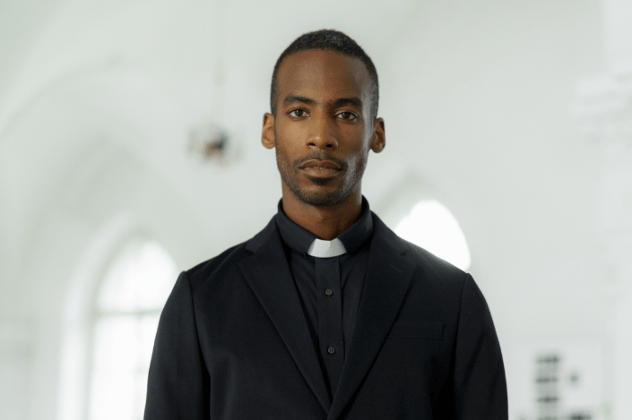 Minister wearing a black suit and white clergy collar.