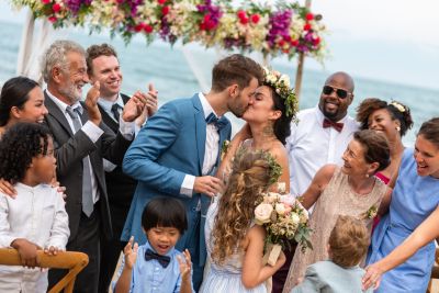 Newly married couple share their first kiss as family and friends celebrate after the wedding ceremony.