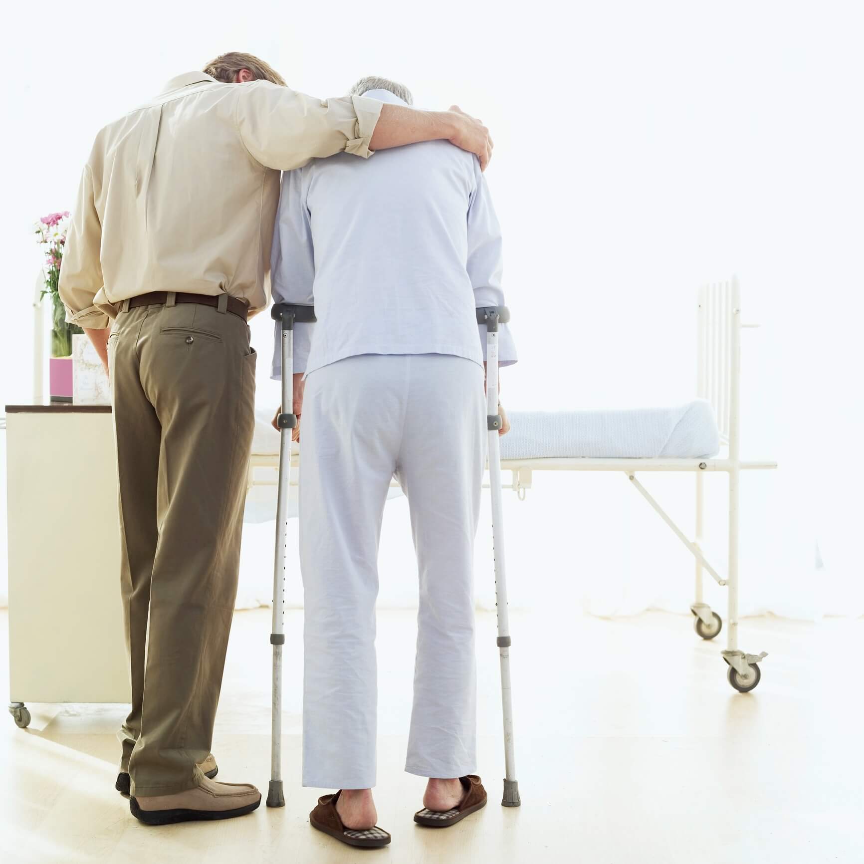 rear view of a son helping his father walk with crutches