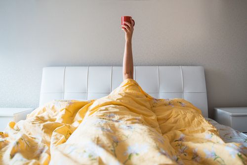 Person Under Covers With Coffee As Morning Routine