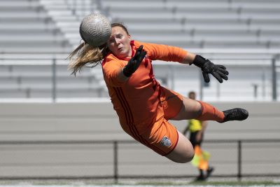 Women's soccer goalkeeper dives to make a save during a competitive match.