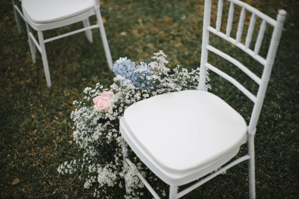 Empty white wedding chair decorated with pink, blue, and white memorial flowers