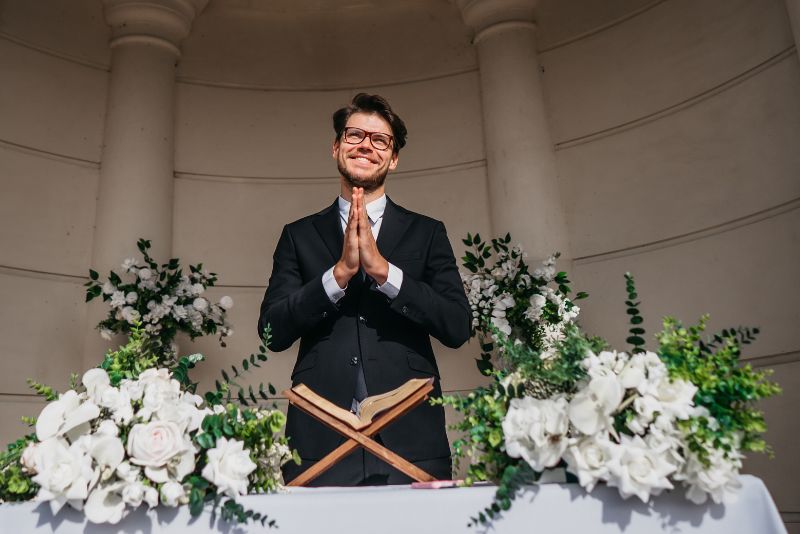 Wedding officiant stands behind a ceremony table with an open book, preparing to officiate a wedding ceremony.