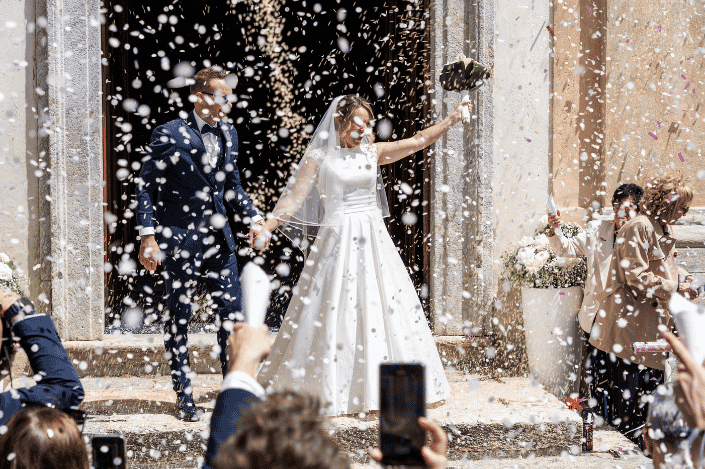 Newly married couple leaving their wedding ceremony as guests shower them with rice and confetti.