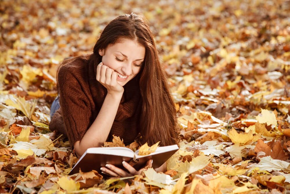 A woman reading scriptures in a pile of autumn leaves.