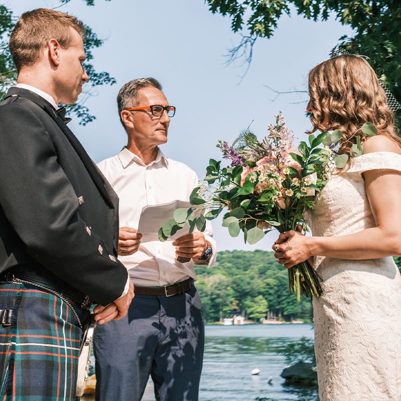 A minister performing an outdoor wedding ceremony on a waterfront.